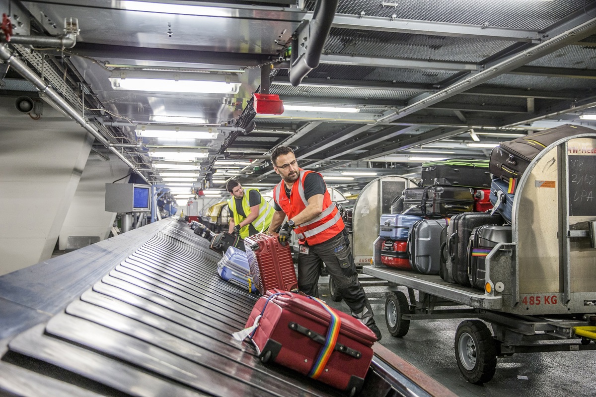 Mitarbeitende verladen Gepäck vom Förderband auf Gepäckwägen