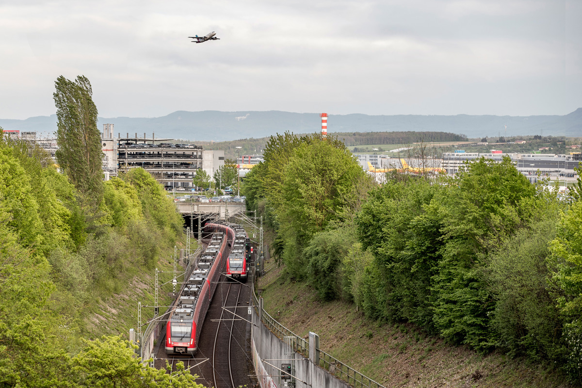 S-Bahn fährt in den Tunnel zum Flughafen ein, im Hintergrund startet ein Flugzeug