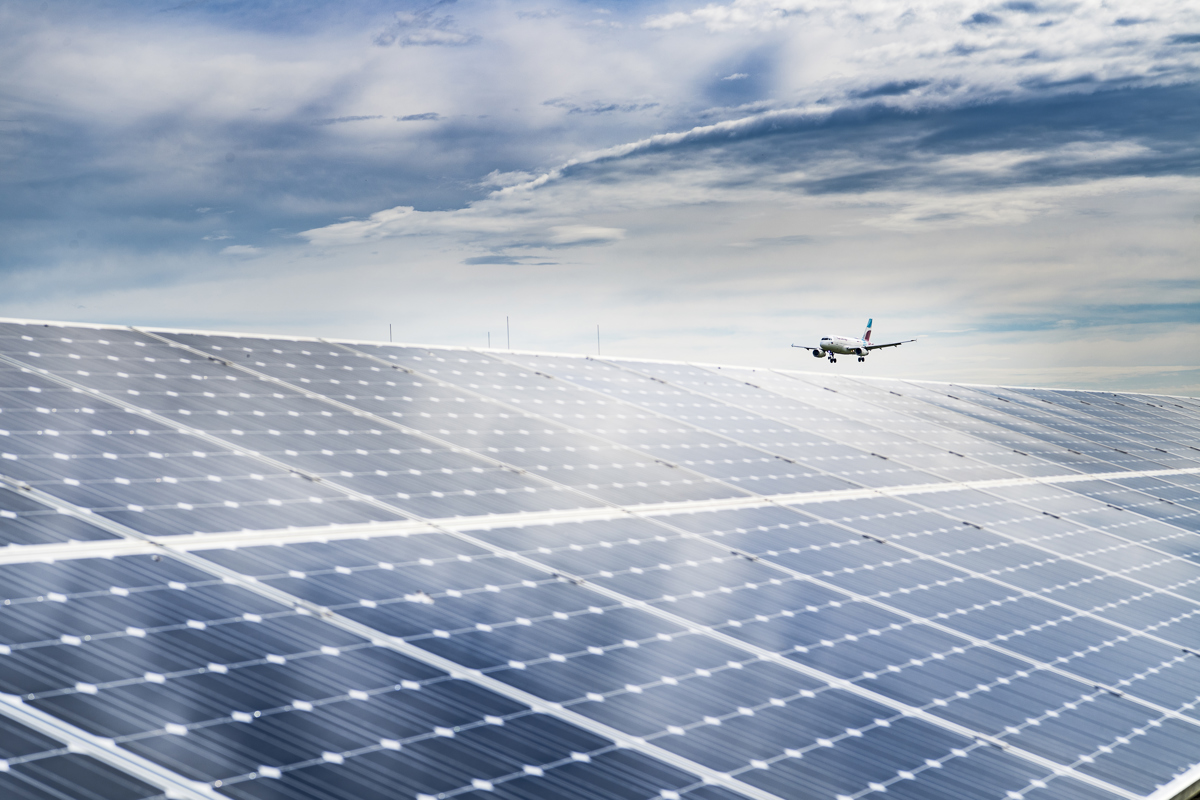 Landende Passagiermaschine hinter einer Solaranlage am Flughafen 