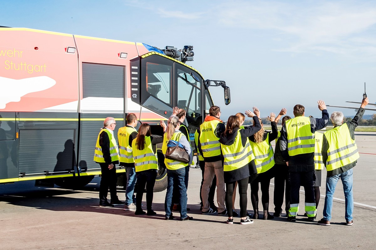 Besuchergruppe auf dem Vorfeld winkt einem Flugzeug